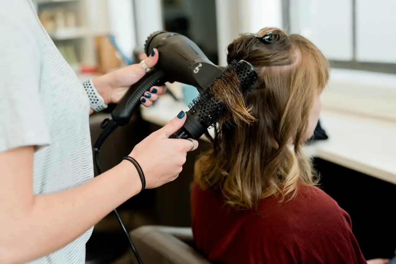 A stylist blow-drying a client’s hair with a round brush