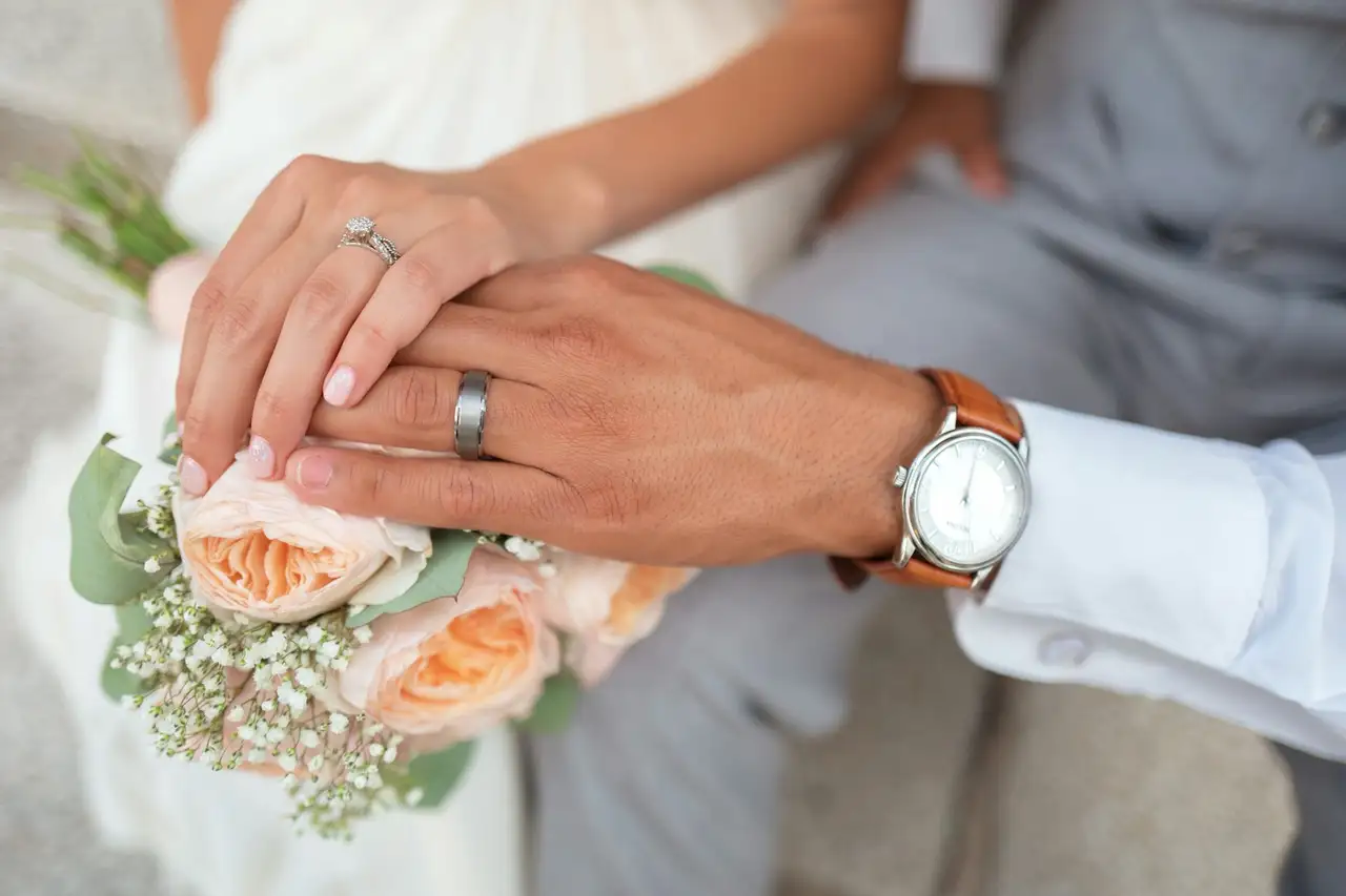 Two hands joined, wedding rings and a small bouquet