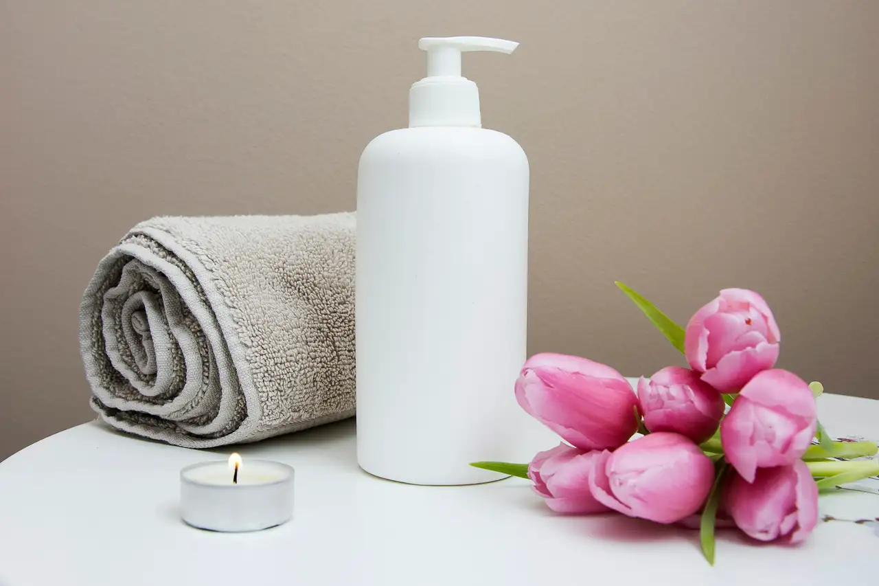 A rolled towel, a bottle and a tea light on a pale surface