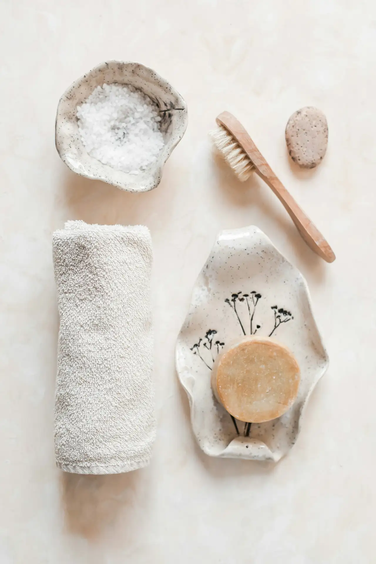 A rolled white towel, a soap dish and a wooden brush on pale linen